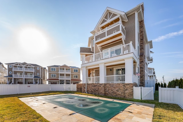 rear view of property with a balcony, a yard, and fence