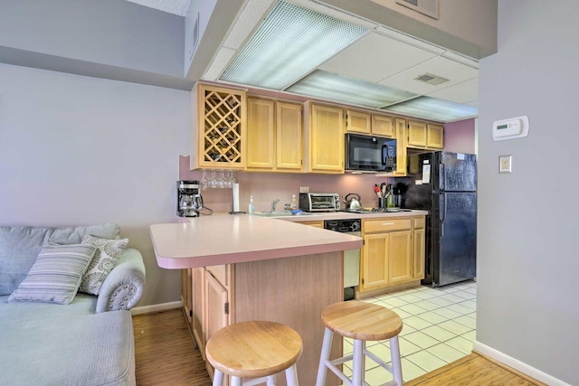 kitchen with light brown cabinetry, sink, a kitchen breakfast bar, kitchen peninsula, and black appliances