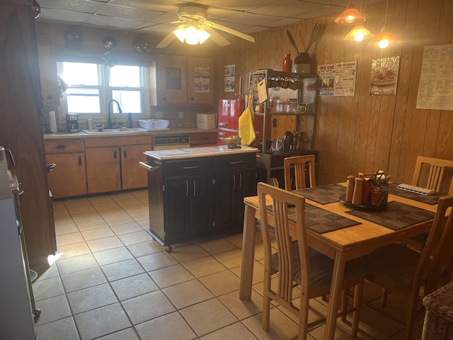 dining area featuring sink, ceiling fan, wood walls, and light tile patterned floors