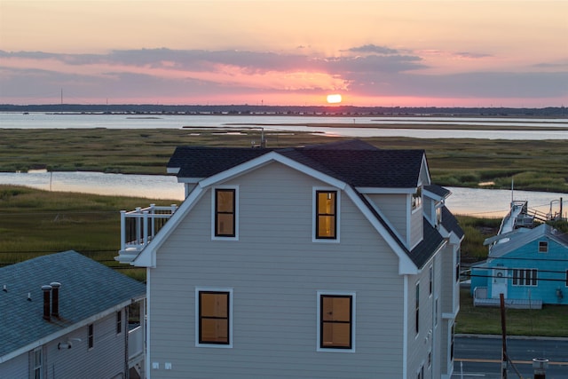 property exterior at dusk featuring a water view and a balcony