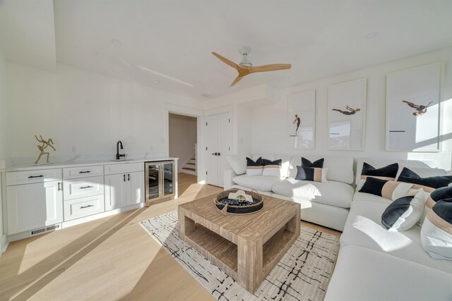 living room with ceiling fan, beverage cooler, sink, and light hardwood / wood-style flooring