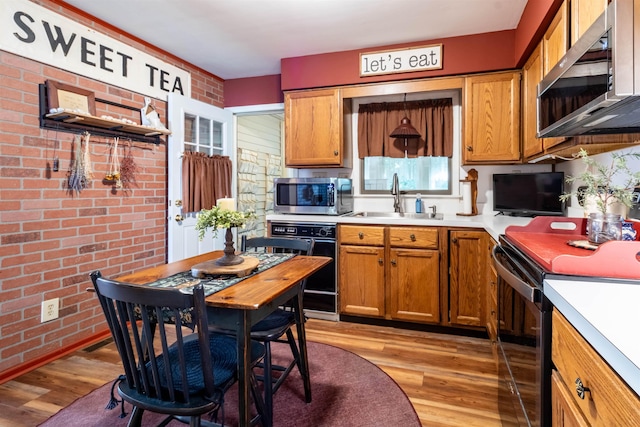 kitchen featuring brick wall, sink, light hardwood / wood-style floors, and black range with electric cooktop