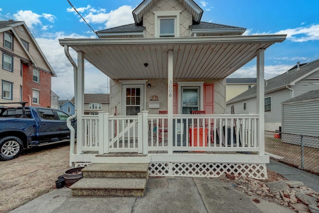 view of front of property featuring a porch, roof with shingles, and fence