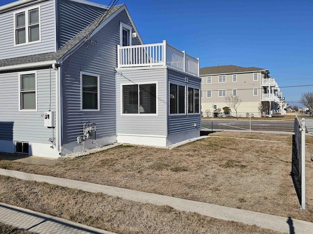 view of side of home with roof with shingles and a balcony