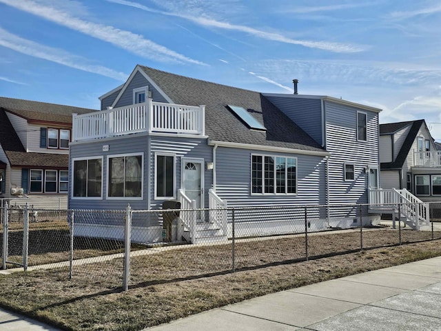 view of front facade with a fenced front yard, a shingled roof, and a balcony