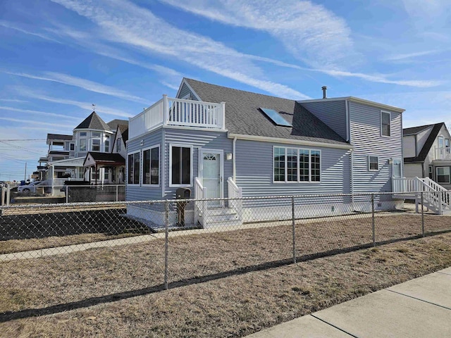 view of front of house with a shingled roof, fence private yard, a balcony, and entry steps