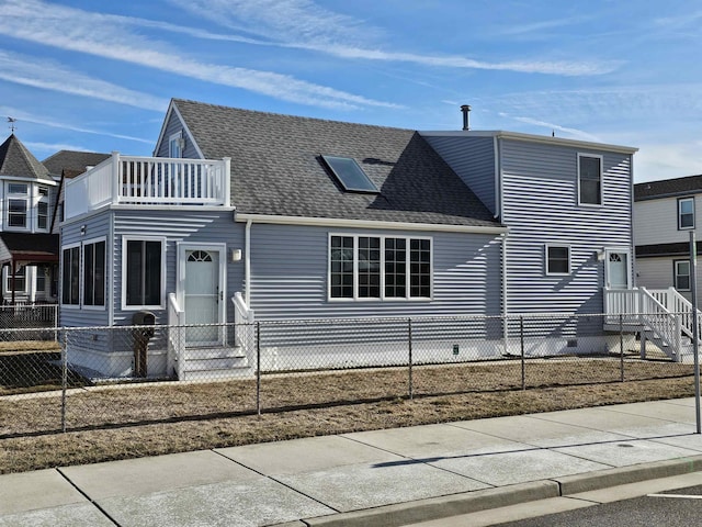 view of front of property featuring a balcony, a fenced front yard, a shingled roof, and crawl space