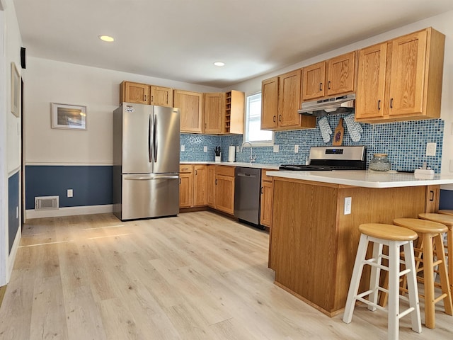 kitchen with visible vents, appliances with stainless steel finishes, a peninsula, light wood-type flooring, and under cabinet range hood