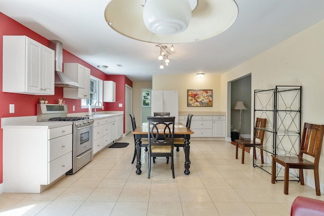 kitchen featuring white cabinets, light countertops, wall chimney range hood, freestanding refrigerator, and gas range