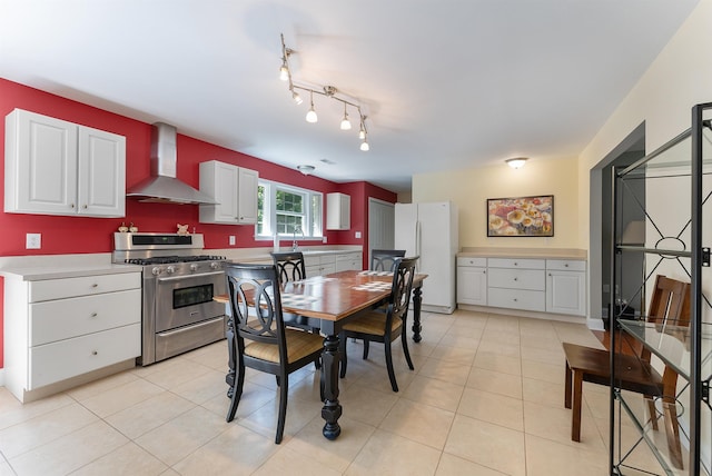 kitchen featuring stainless steel gas stove, wall chimney exhaust hood, white cabinets, and freestanding refrigerator