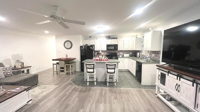 kitchen with a center island, black appliances, dark hardwood / wood-style floors, a kitchen bar, and white cabinetry