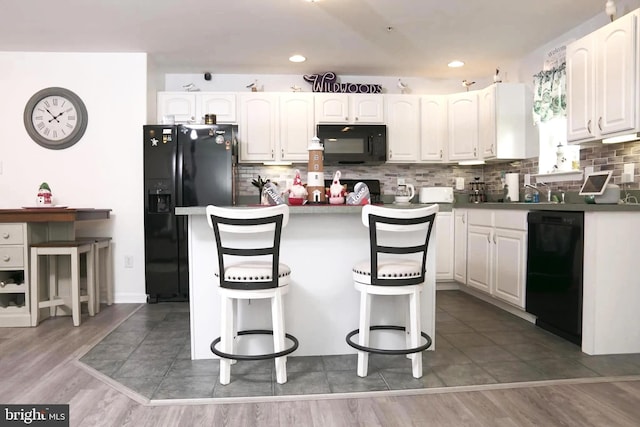 kitchen featuring black appliances, dark hardwood / wood-style flooring, white cabinets, and a kitchen bar