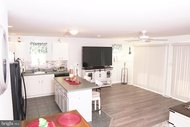 kitchen with a center island, backsplash, black fridge, white cabinetry, and a breakfast bar area