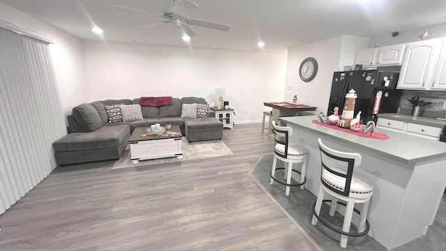 kitchen with a kitchen bar, black fridge with ice dispenser, ceiling fan, wood-type flooring, and white cabinetry