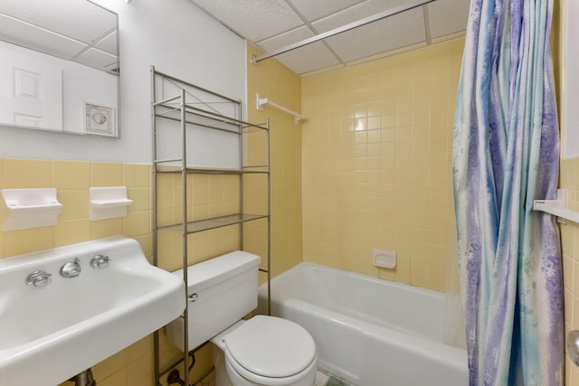 full bathroom with toilet, tile walls, a drop ceiling, sink, and shower / tub combo with curtain