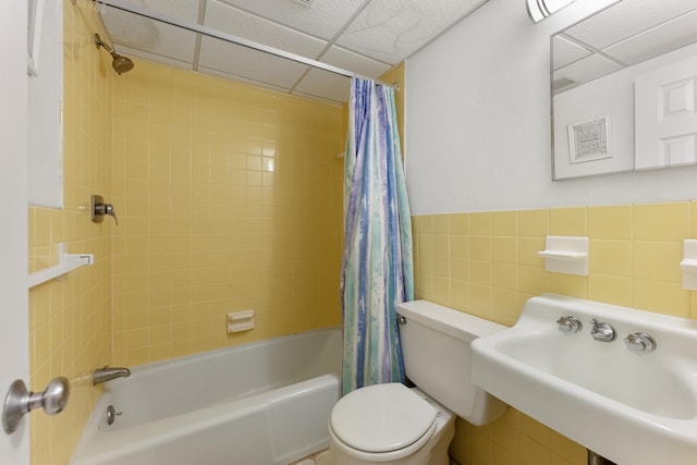 full bathroom featuring toilet, a paneled ceiling, shower / tub combo with curtain, tile walls, and sink