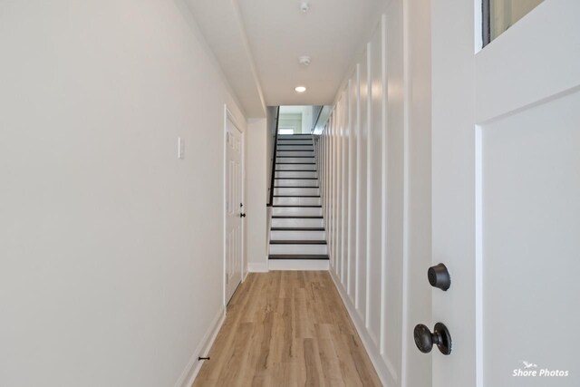 hallway with light wood-style floors, baseboards, and stairs