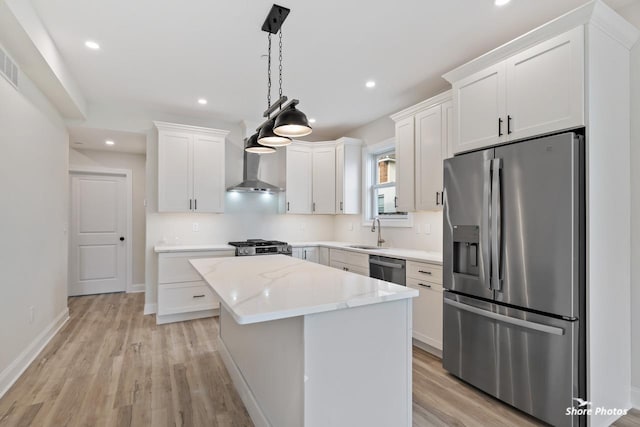 kitchen with appliances with stainless steel finishes, a sink, wall chimney range hood, a kitchen island, and white cabinetry