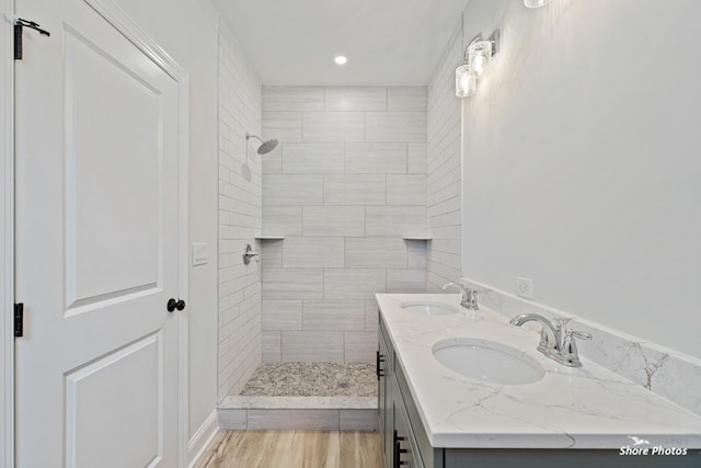 full bath with tiled shower, wood finished floors, recessed lighting, and double vanity
