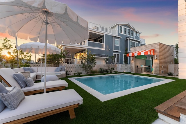 pool at dusk featuring a yard and outdoor lounge area