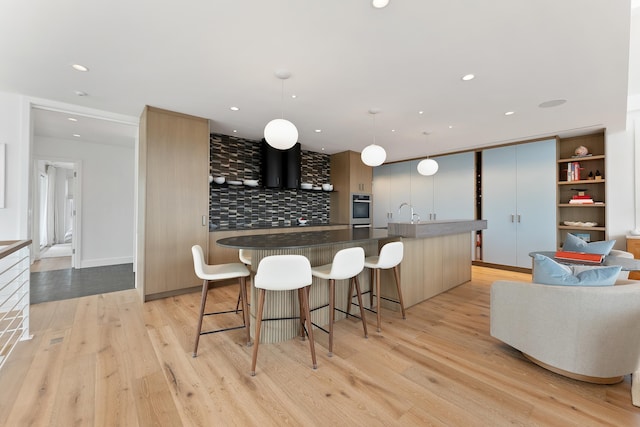 kitchen with pendant lighting, tasteful backsplash, an island with sink, a kitchen bar, and light hardwood / wood-style flooring