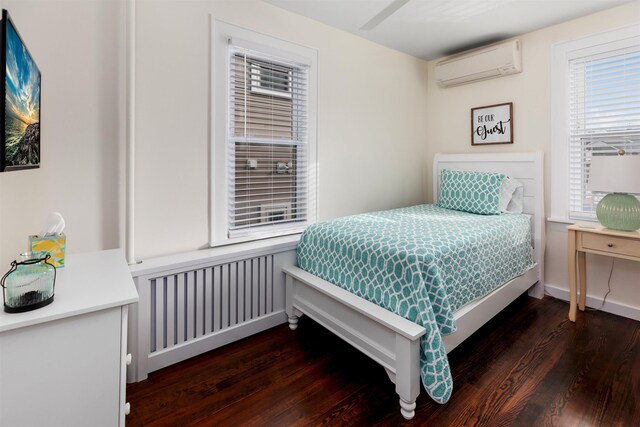 bedroom with a wall mounted air conditioner, baseboards, and wood finished floors