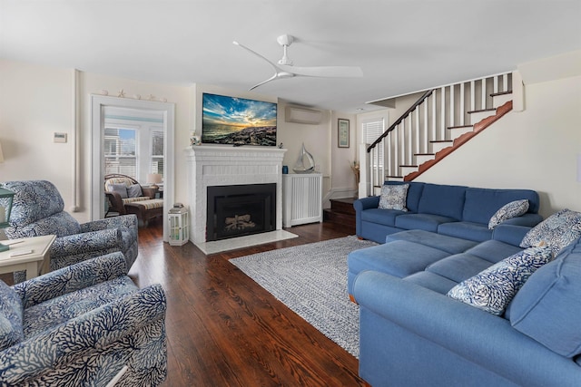 living room featuring ceiling fan, a fireplace with flush hearth, wood finished floors, an AC wall unit, and stairs