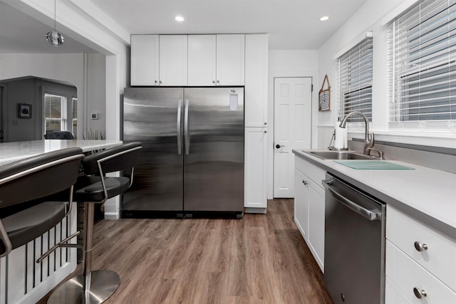 kitchen featuring white cabinets, a sink, light countertops, appliances with stainless steel finishes, and wood finished floors