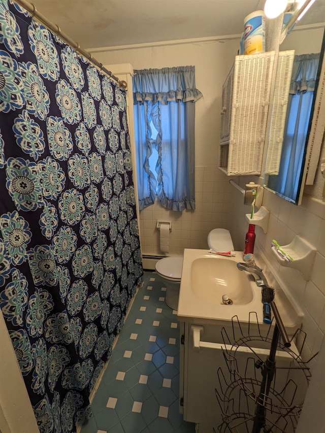 bathroom with baseboard heating, toilet, decorative backsplash, vanity, and tile walls