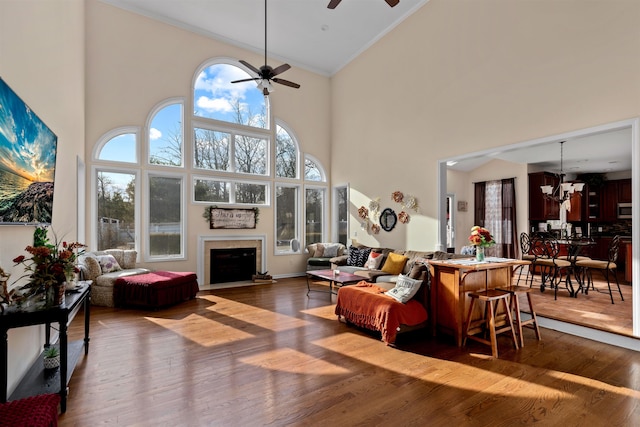 living room featuring dark wood-style floors, a wealth of natural light, a fireplace, and ceiling fan with notable chandelier