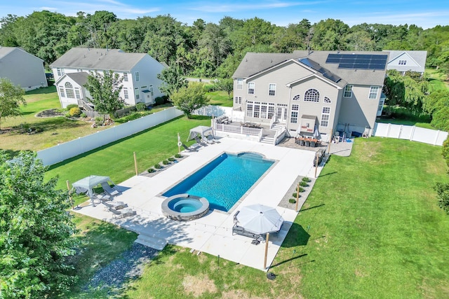 back of property with a lawn, a swimming pool with hot tub, a patio, and solar panels