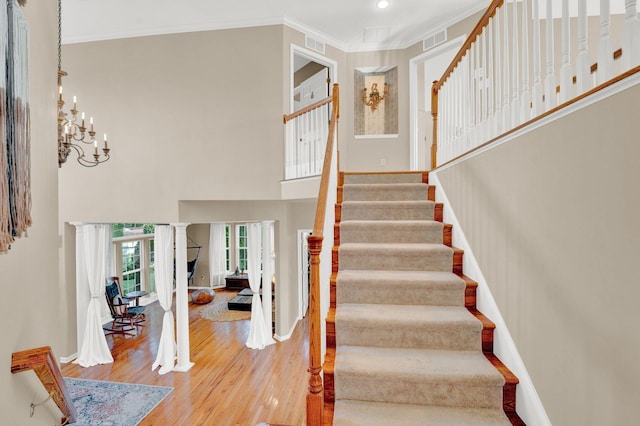 stairway featuring decorative columns, wood-type flooring, a notable chandelier, and ornamental molding