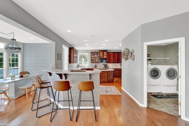 kitchen featuring light hardwood / wood-style flooring, a notable chandelier, kitchen peninsula, a kitchen bar, and washer and dryer