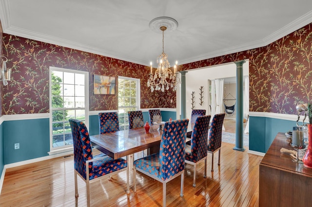 dining room with a notable chandelier, wood-type flooring, ornate columns, and crown molding