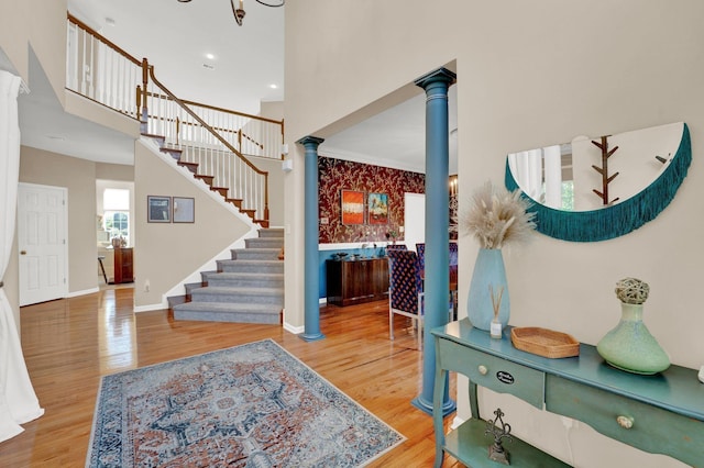 foyer featuring wood-type flooring, a towering ceiling, and ornate columns