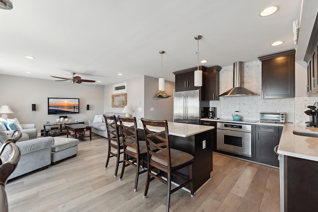 kitchen with a kitchen bar, stainless steel appliances, wall chimney range hood, pendant lighting, and a center island