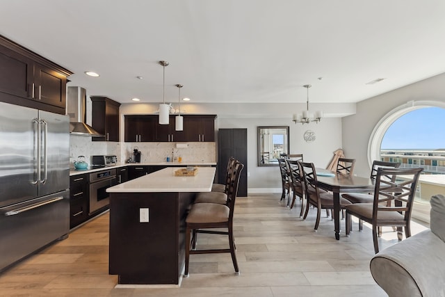 kitchen with a center island, wall chimney exhaust hood, hanging light fixtures, and appliances with stainless steel finishes