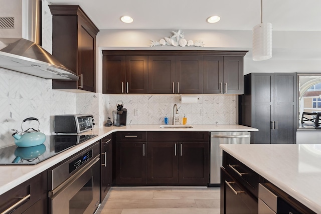 kitchen with wall chimney range hood, hanging light fixtures, sink, decorative backsplash, and appliances with stainless steel finishes