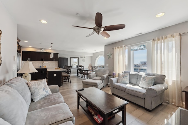 living room with ceiling fan with notable chandelier and light wood-type flooring