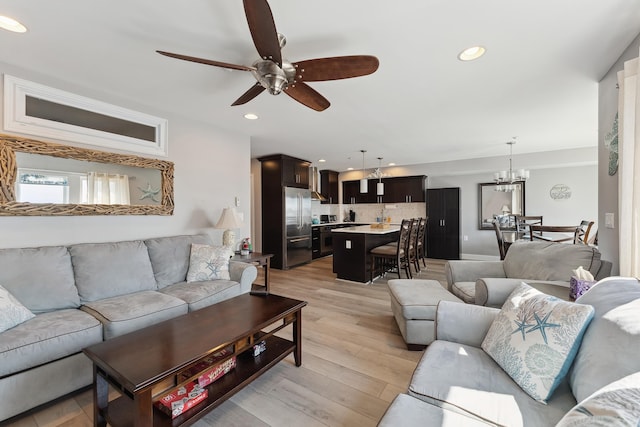 living room with ceiling fan with notable chandelier and light wood-type flooring