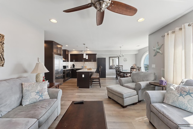 living room featuring ceiling fan with notable chandelier and light hardwood / wood-style floors