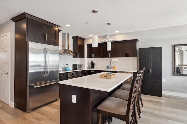 kitchen with a center island, wall chimney exhaust hood, stainless steel appliances, light hardwood / wood-style flooring, and decorative light fixtures