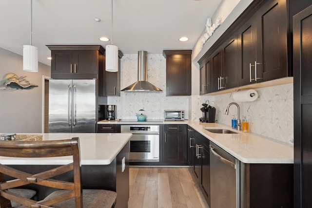 kitchen featuring wall chimney range hood, sink, decorative light fixtures, a kitchen bar, and stainless steel appliances