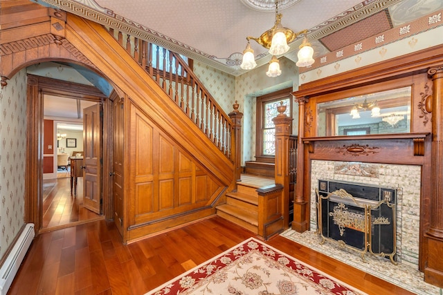 645 Hughes St, Cape May, NJ 08204 - stairway with wallpapered walls, baseboard heating, a chandelier, wood finished floors, and a fireplace with flush hearth