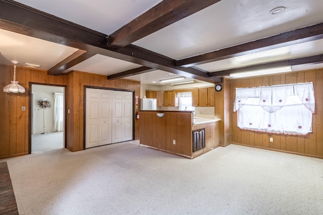 kitchen with brown cabinets, a peninsula, beamed ceiling, wood walls, and freestanding refrigerator