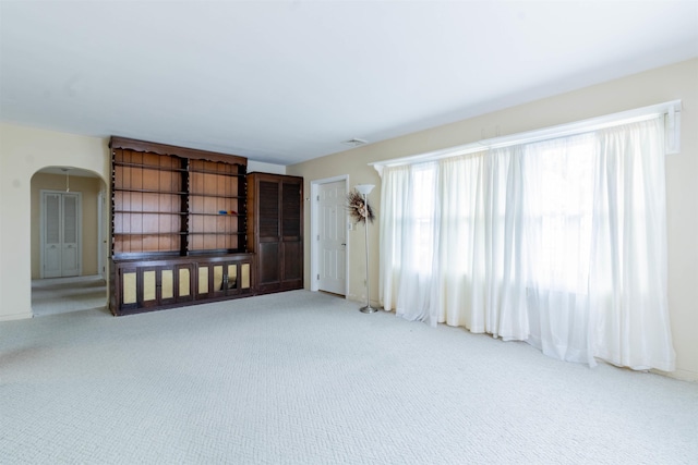 carpeted empty room with arched walkways and visible vents