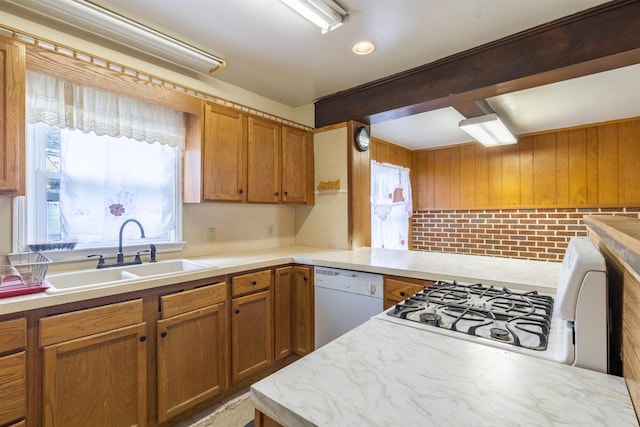 kitchen featuring white dishwasher, a sink, cooktop, brown cabinets, and a peninsula