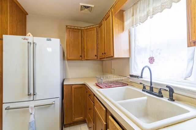 kitchen featuring a sink, visible vents, freestanding refrigerator, brown cabinets, and light countertops