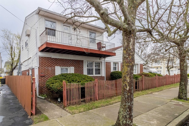 view of front facade with brick siding, a balcony, and a fenced front yard