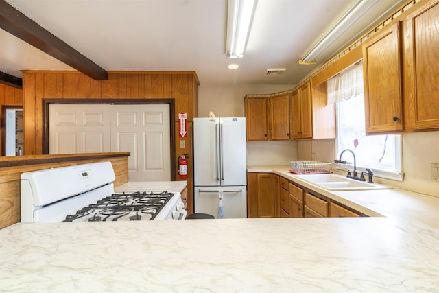 kitchen featuring wood walls, visible vents, a sink, beamed ceiling, and white appliances